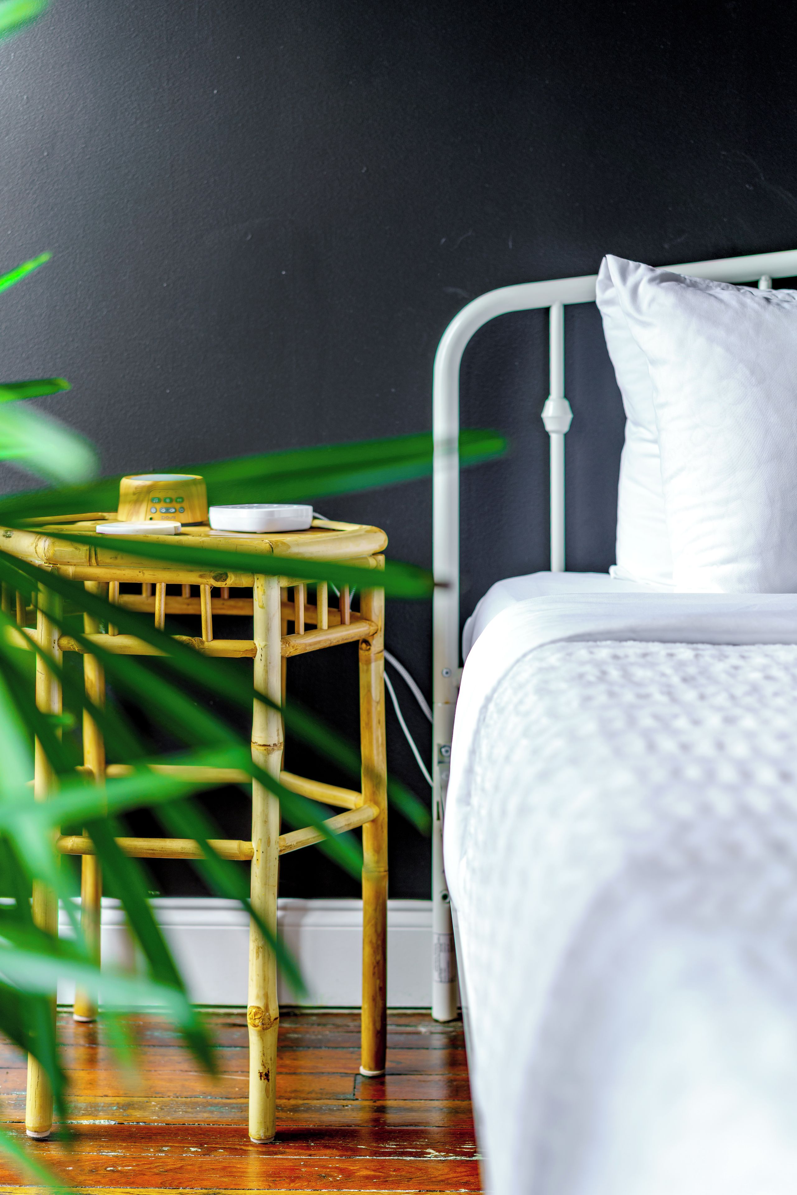 A bed with white bedding, a bedside table with a small appliance, and a bamboo stool.