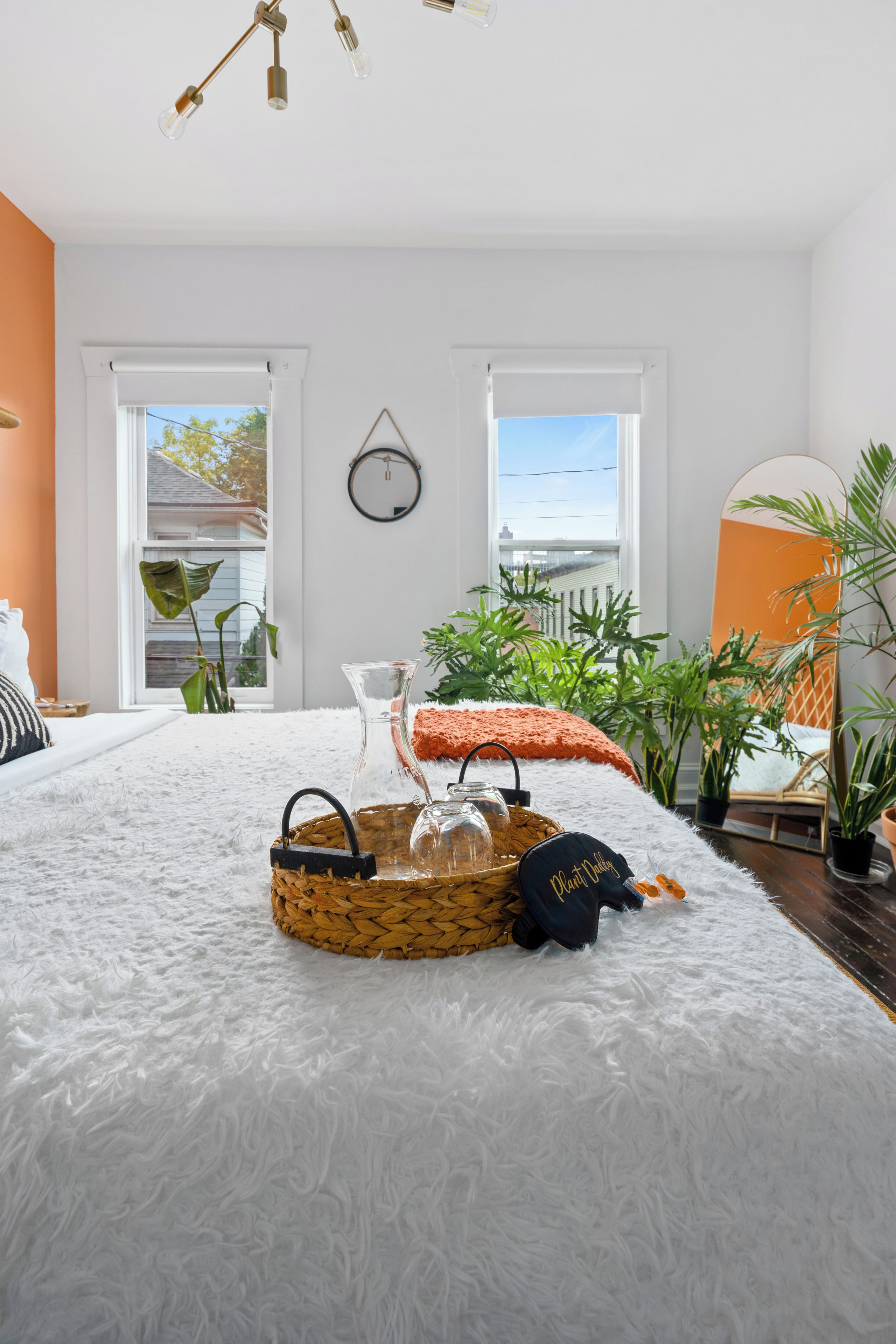 A bedroom with a large bed, a white furry rug, a wicker basket, a glass vase, and a mirror.