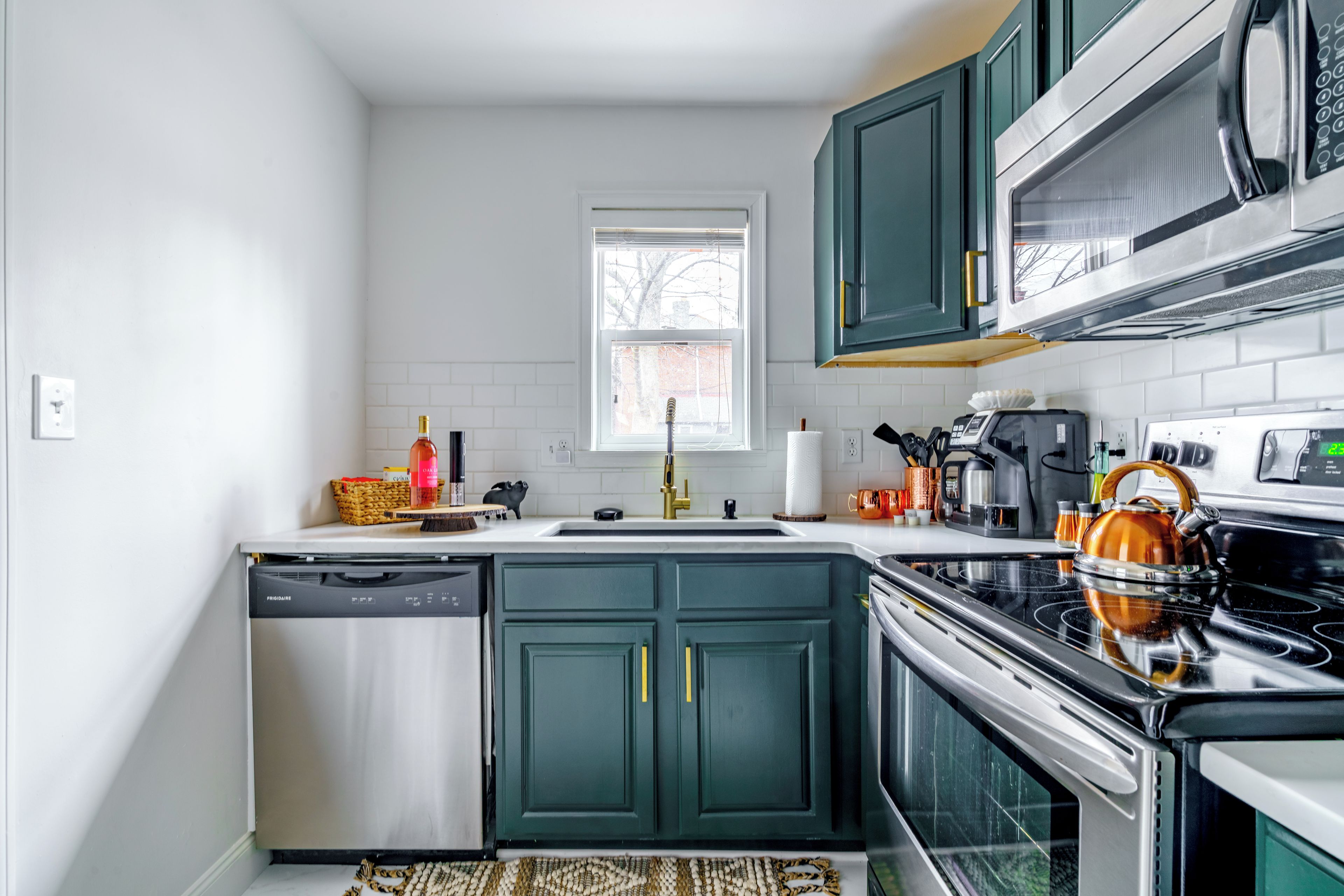 A compact kitchen with a dishwasher, stove, microwave, and green cabinets.