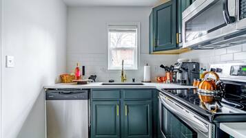 A compact kitchen with a dishwasher, stove, microwave, and green cabinets.