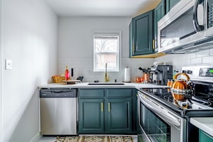 A compact kitchen with a dishwasher, stove, microwave, and green cabinets.