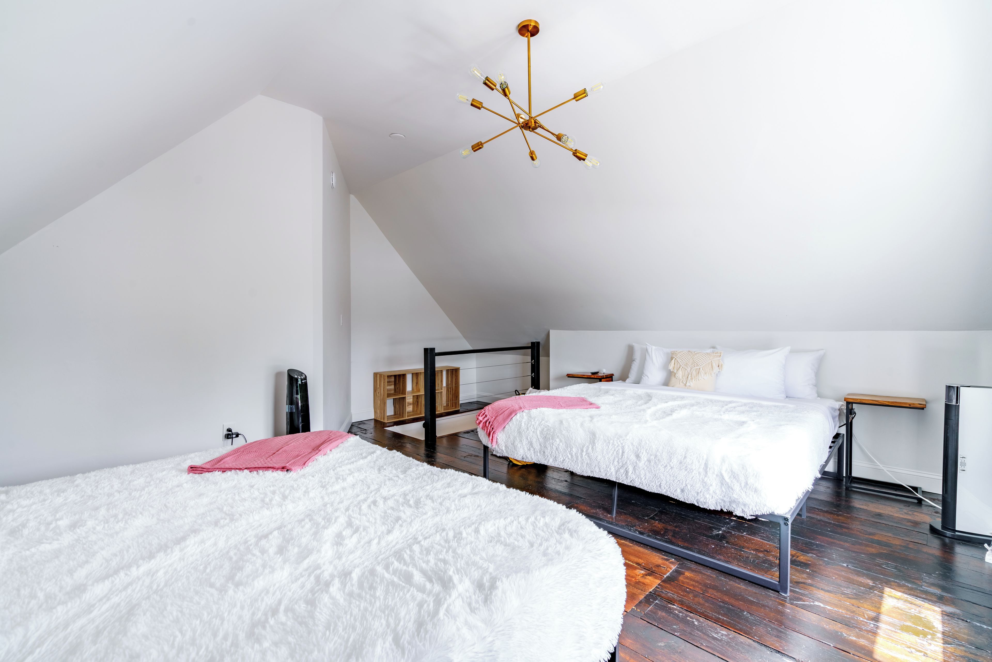 A modern bedroom with two beds, a wooden floor, a sloped ceiling, and a unique chandelier.