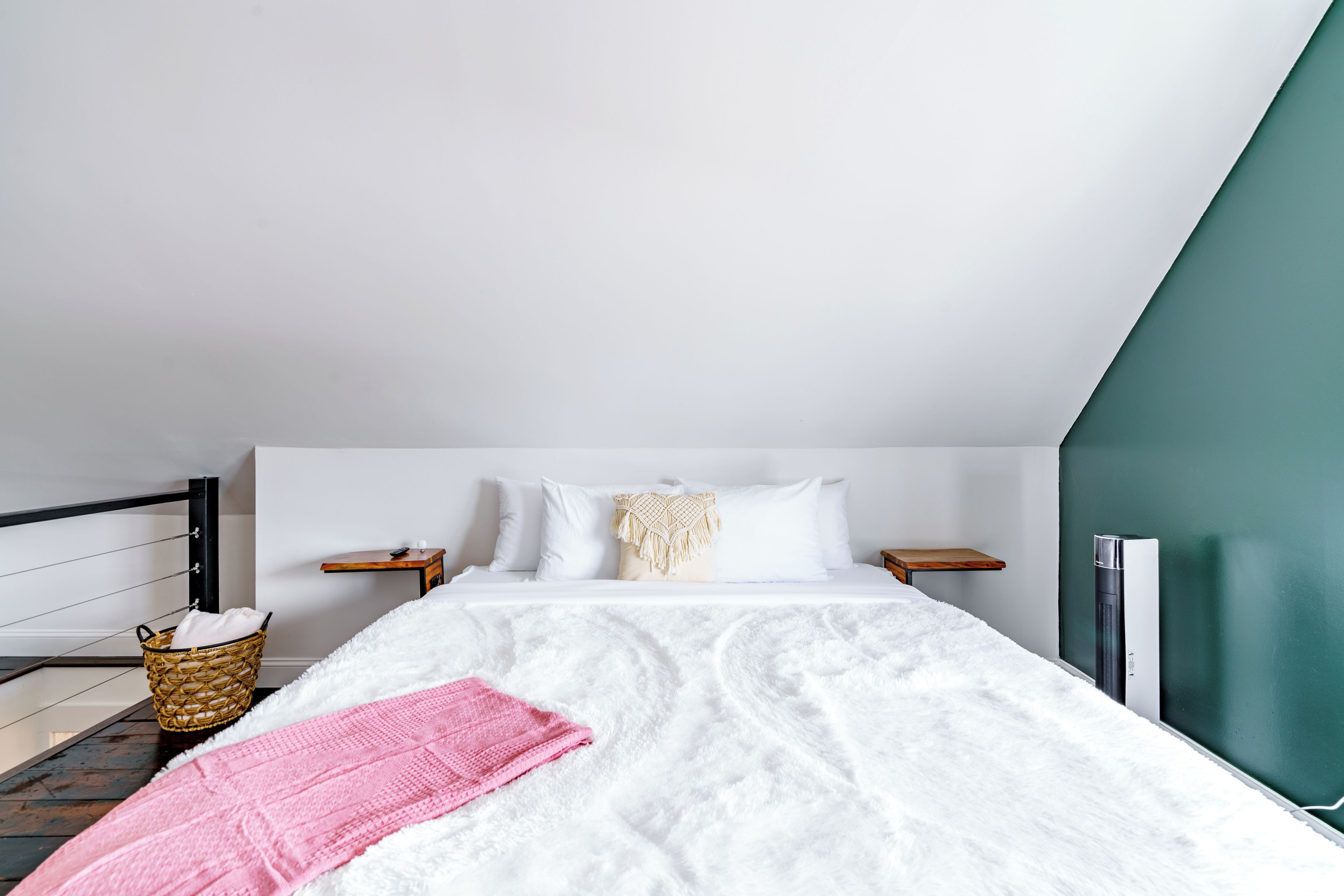Une chambre avec un lit blanc, une couverture rose, un panier en osier et un mur vert.