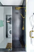 Un baño moderno con ducha, un perchero y una lavadora al fondo.