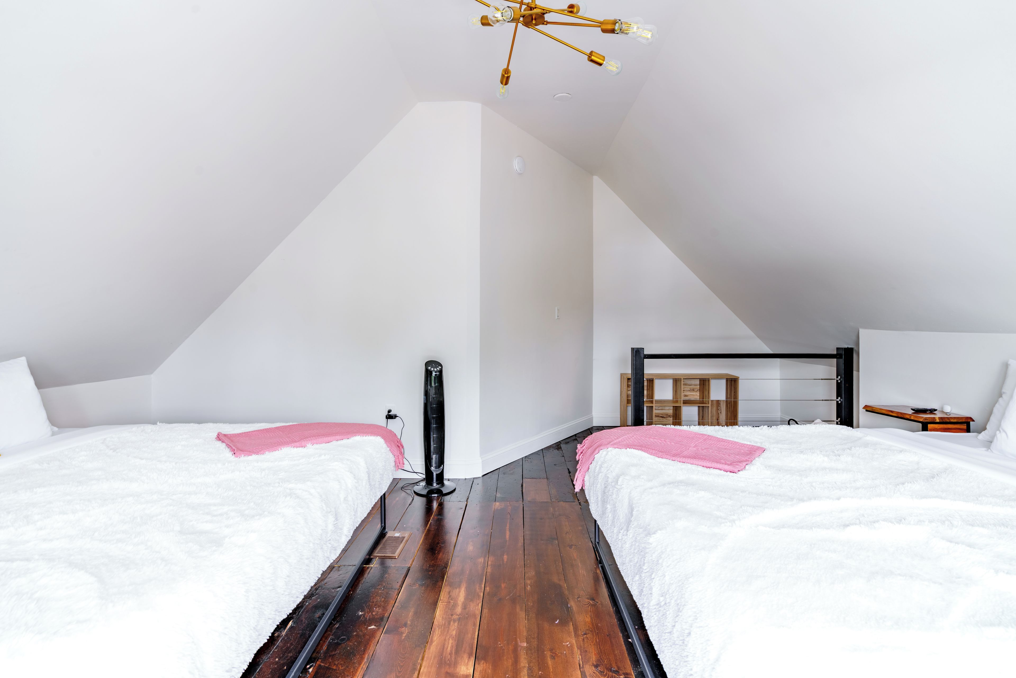 A bedroom with two beds, a wooden floor, a ceiling fan, and a small bedside table.
