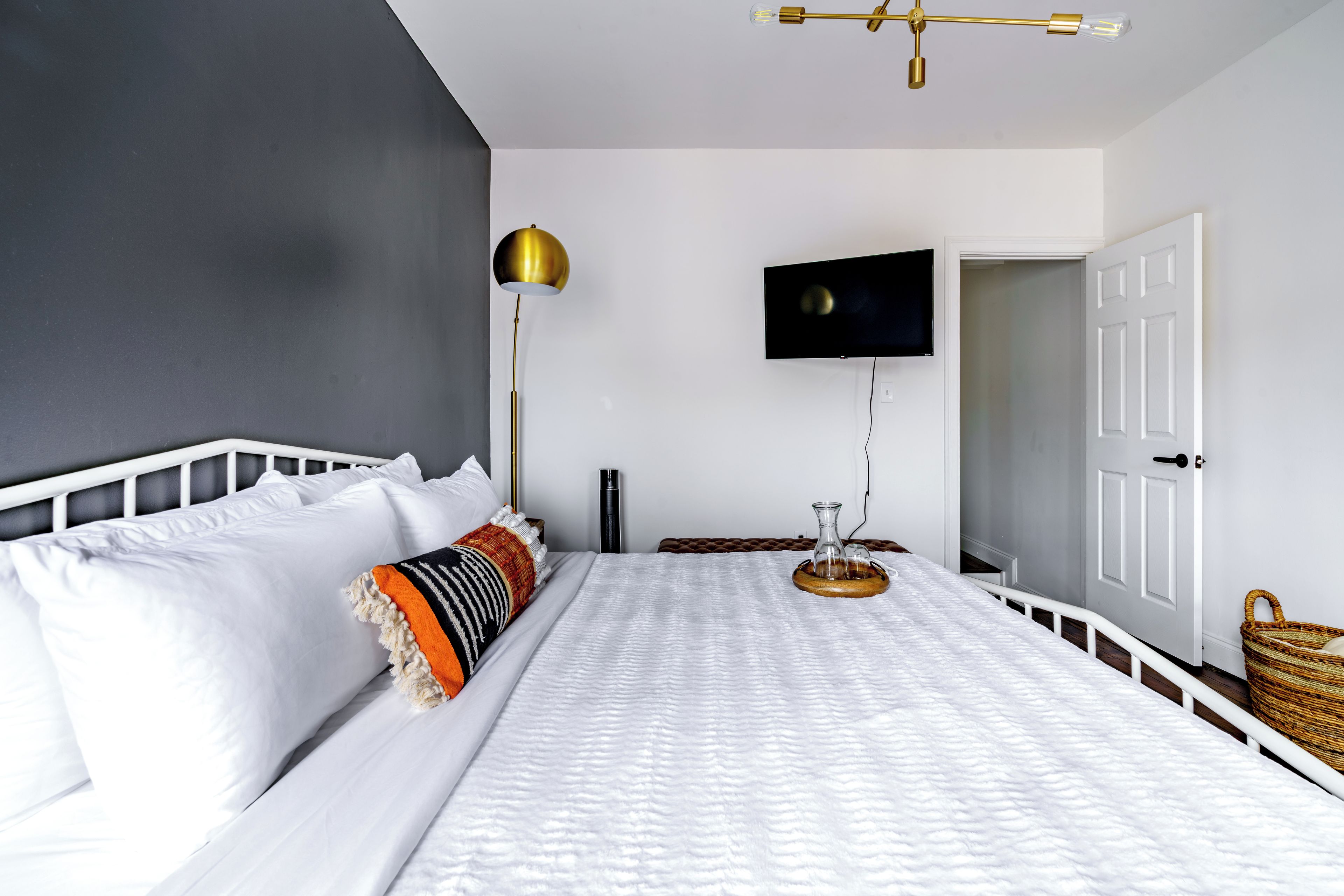 Un dormitorio con cama, lámpara de noche, televisor montado en la pared y una puerta.