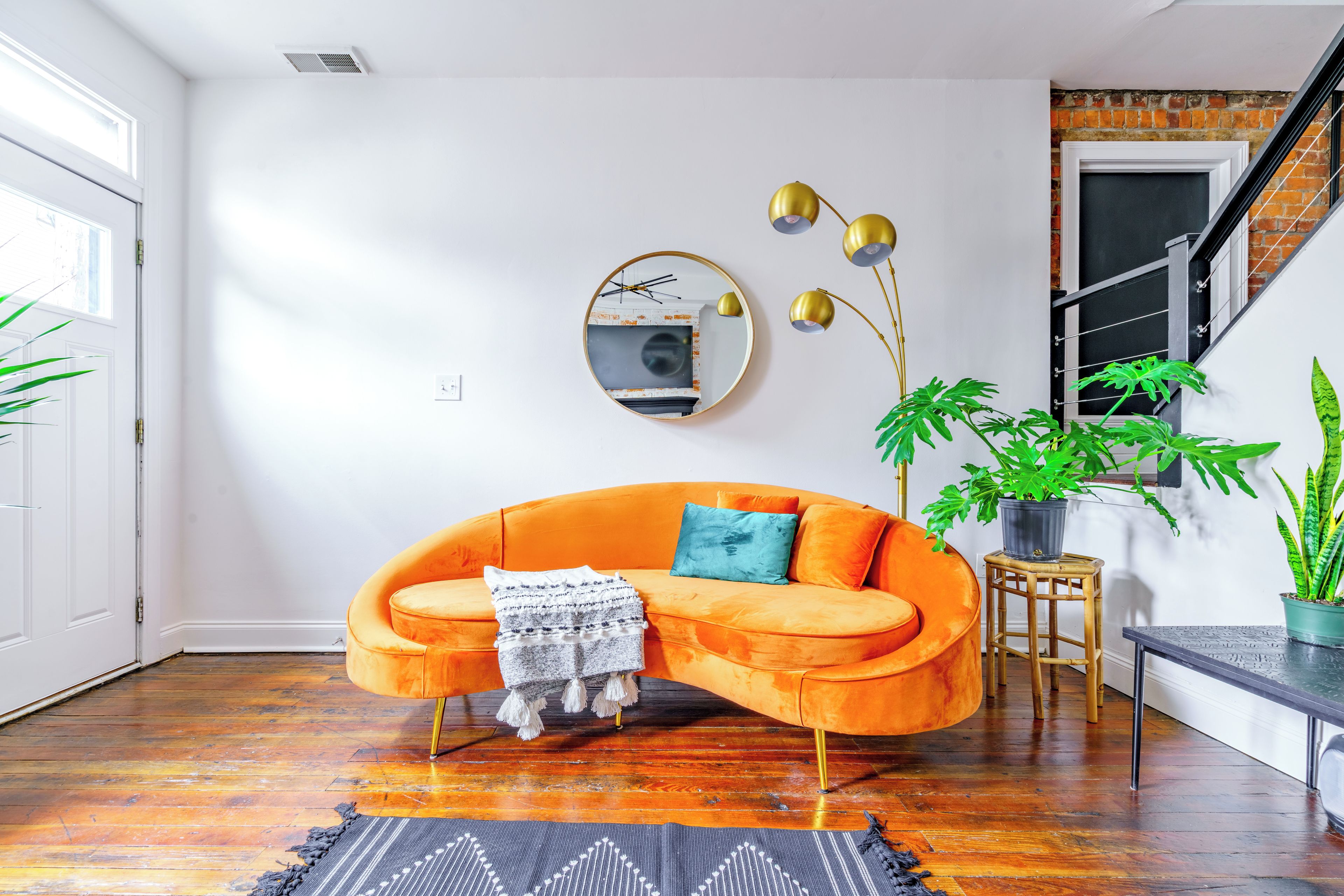 En moderne stue med en levende orange sofa, et rundt spejl og en trappe med en murstensvæg.
