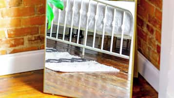 A mirror reflecting a room with a brick wall, a white radiator, a green plant, and a white baby crib.