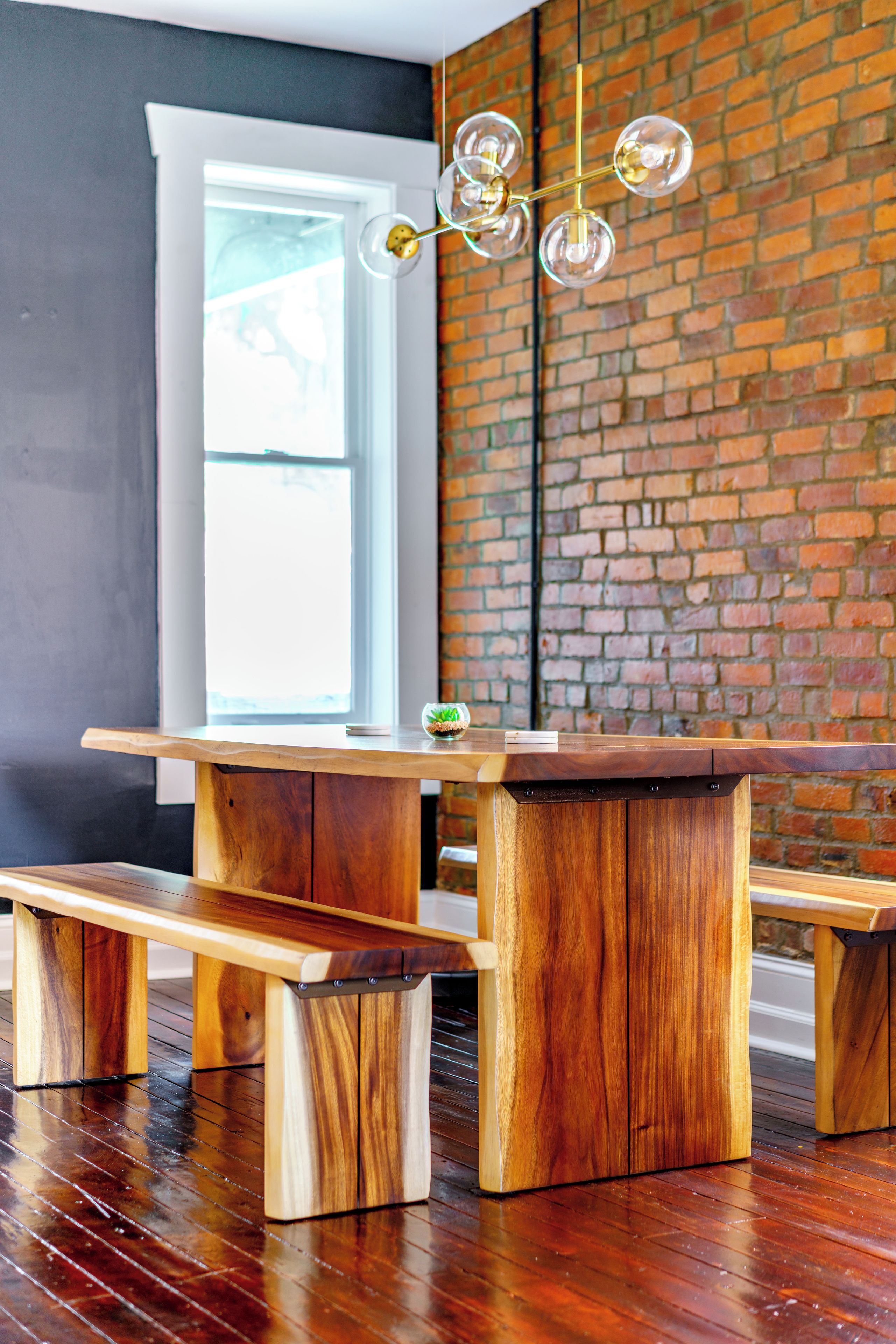 Een houten tafel met banken, een bakstenen muur en een hanglamp.