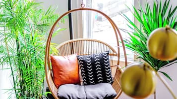 A room with a hanging chair, potted plants, and a window with blinds.