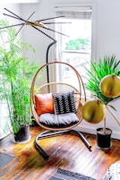 Una habitación con una silla colgante, plantas en macetas y una ventana con persianas.