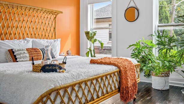 A bed with a white fluffy cover, a woven headboard, and a bedside table with a plant and a lamp. - Jungle House Urban Lofts - Short North & Convention Center (Columbus)