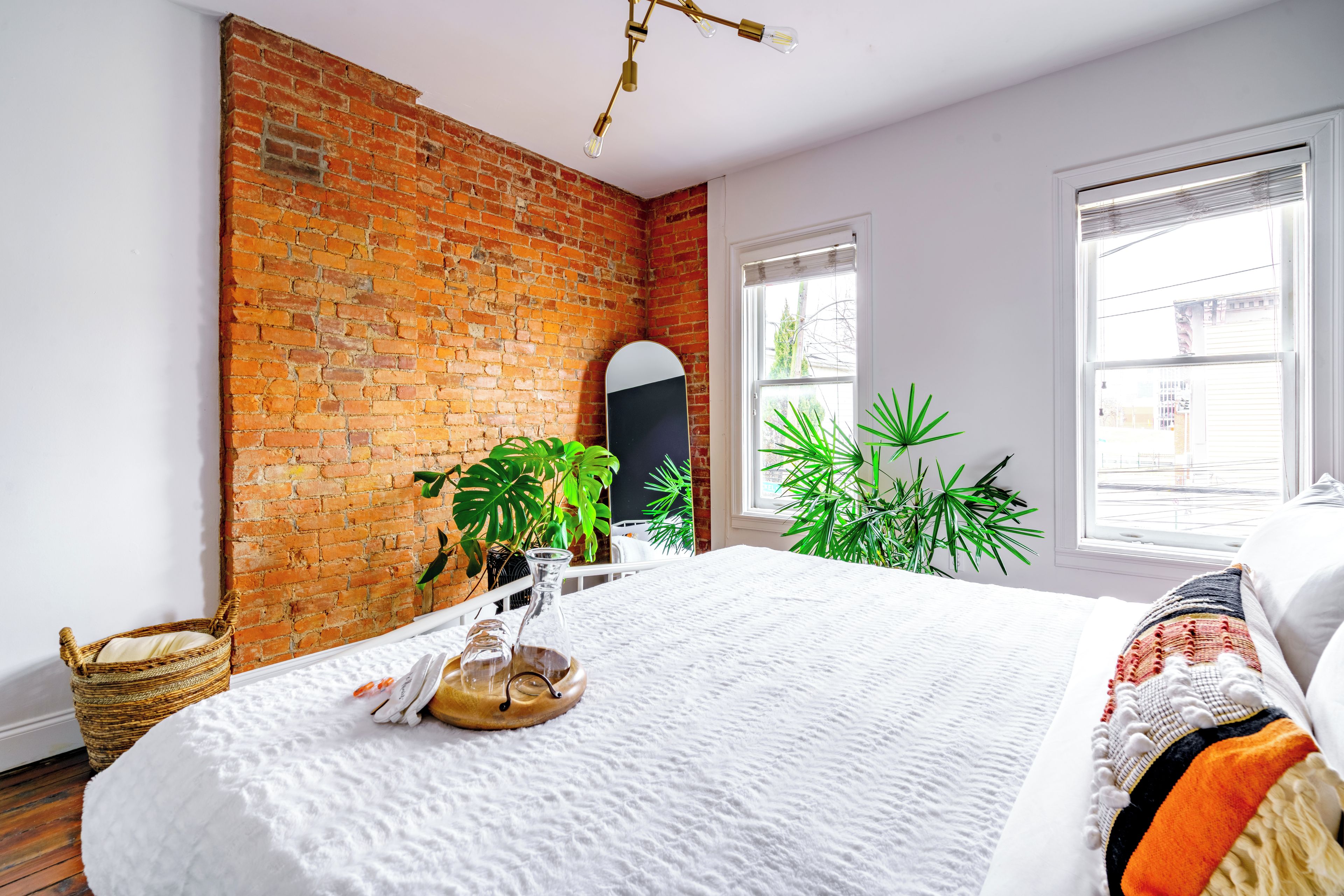 Een kamer met een bakstenen muur, een bed met witte lakens, een raam met zonwering en een plant.