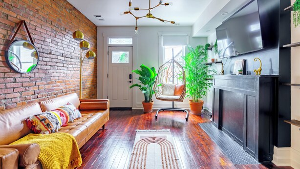 A modern living room with a brick wall, leather sofa, hanging chair, and a large TV. - Jungle House Urban Lofts - Short North & Convention Center (Columbus)