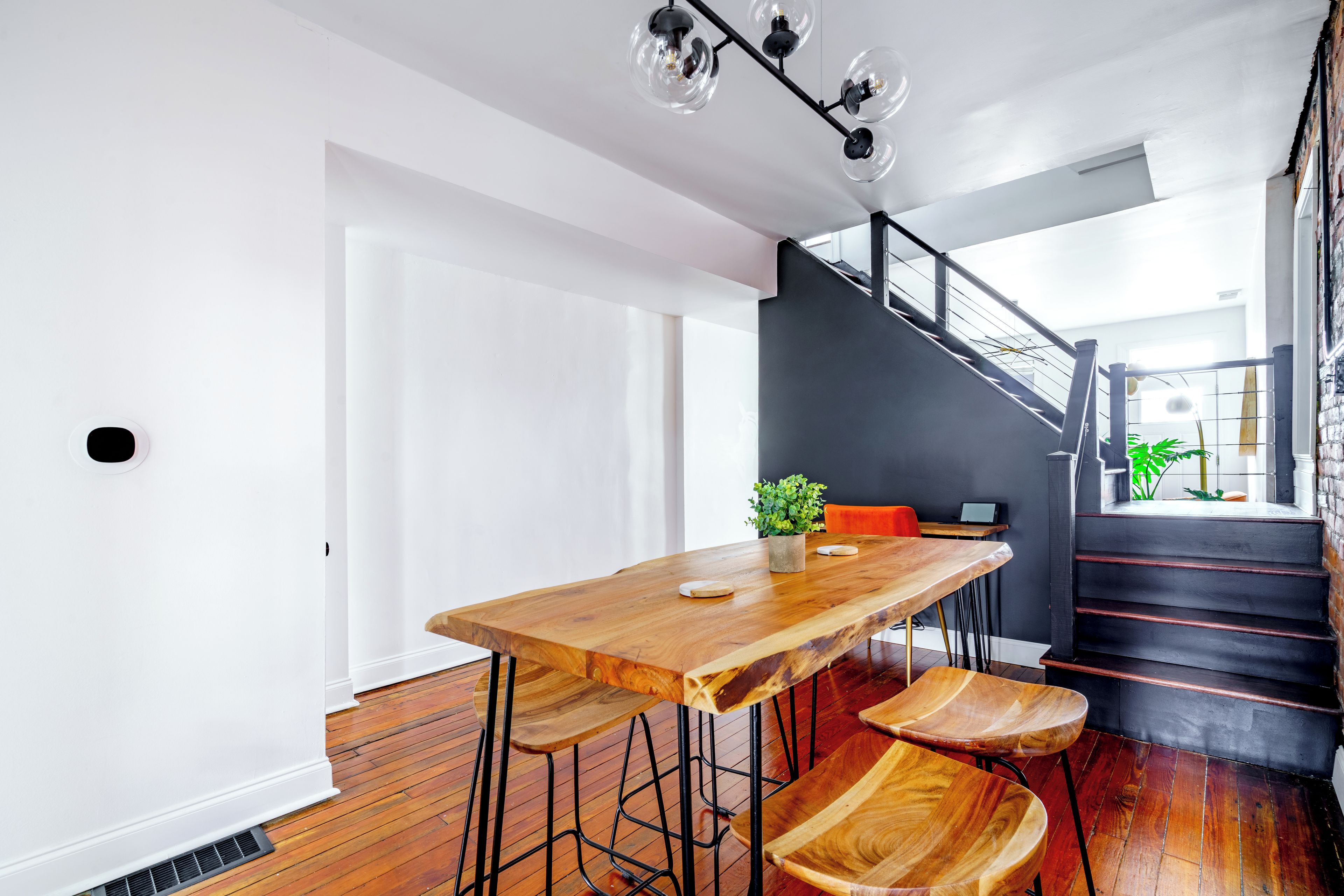 A modern interior with a wooden dining table, chairs, a staircase, and a plant.