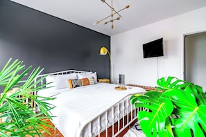 Camera da letto con un letto, un comodino, una lampada, una TV e una pianta verde grande.