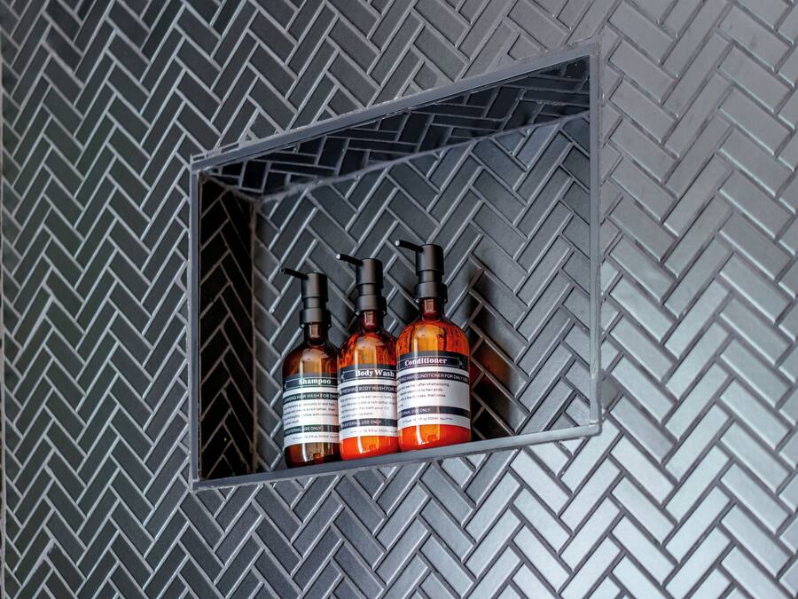 Une étagère en métal sur laquelle sont posées trois bouteilles de gel douche et d’après-shampoing.