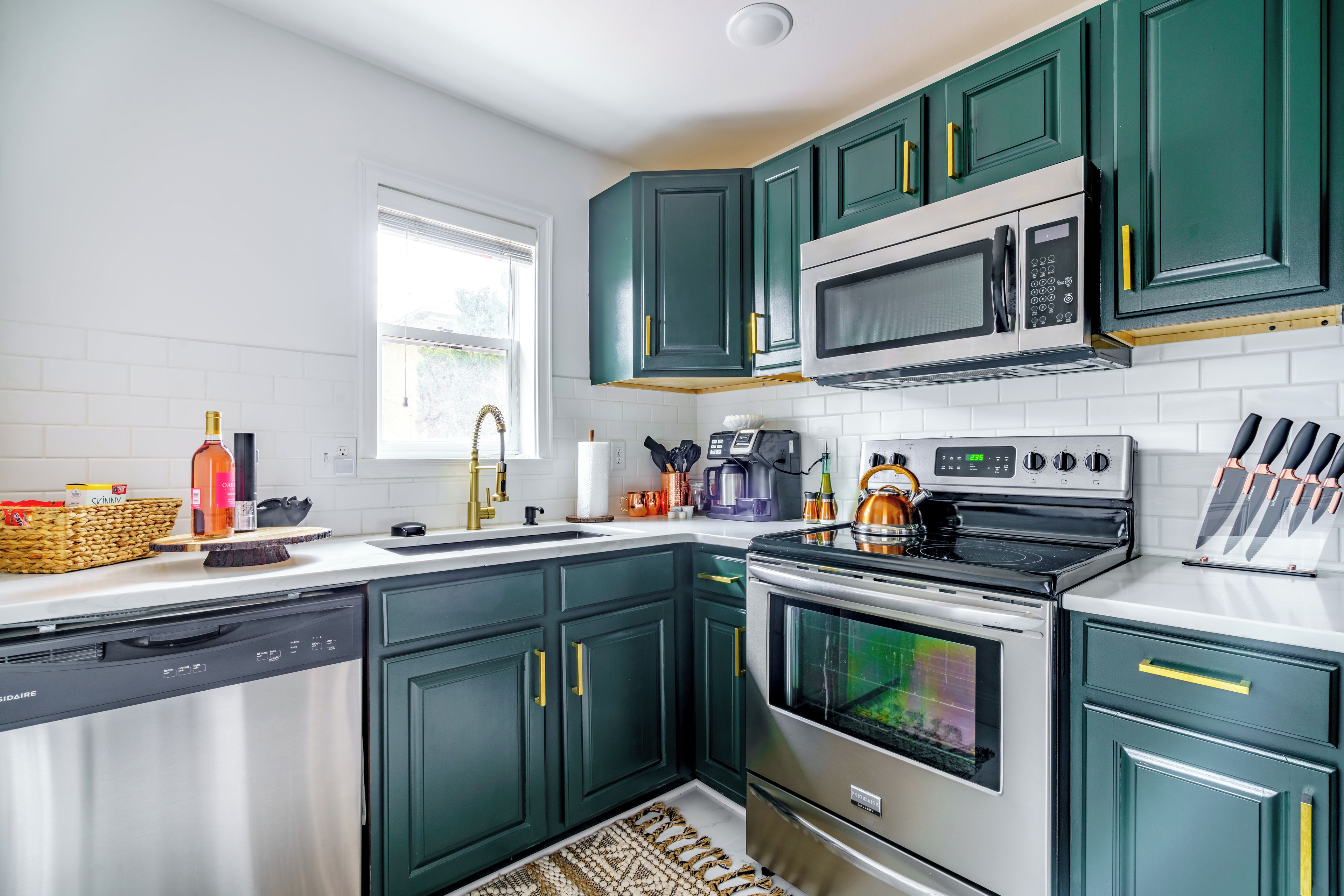 Une cuisine moderne avec des meubles de couleur vert foncé, des appareils en acier inoxydable et un dosseret de carrelage blanc.