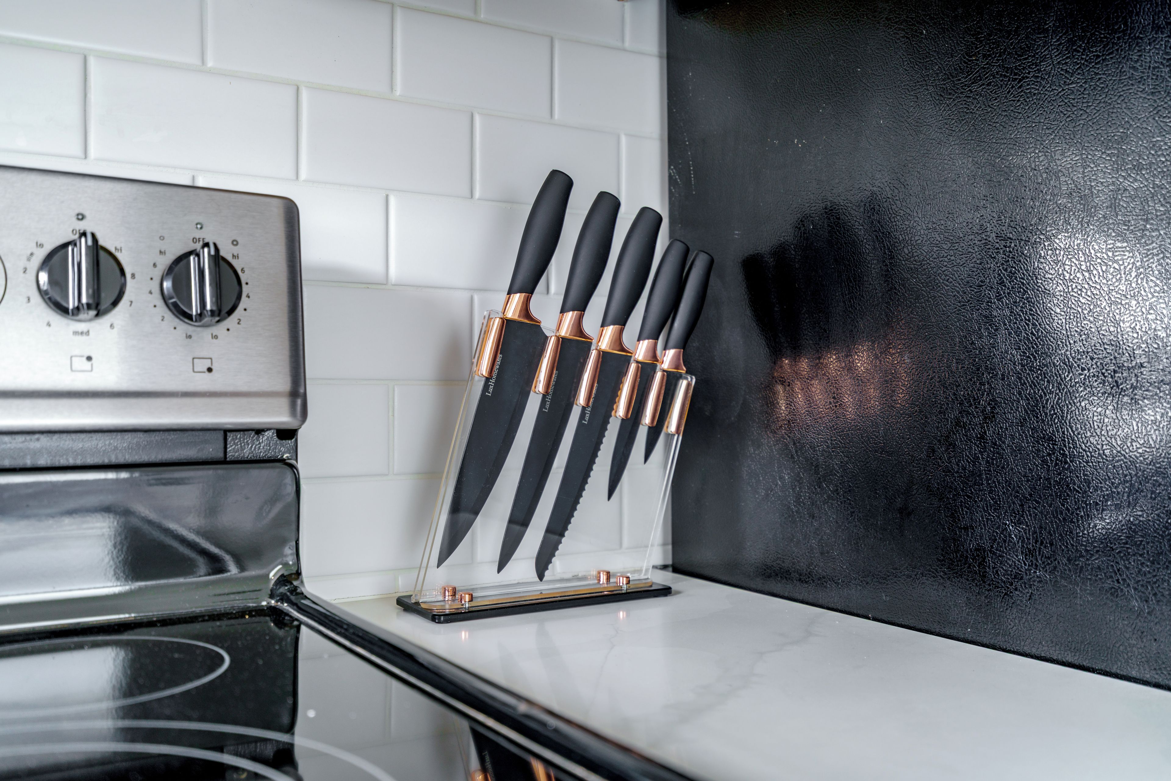 Una cocina con estufa de acero inoxidable, un bloque de cuchillos y un salpicadero negro.