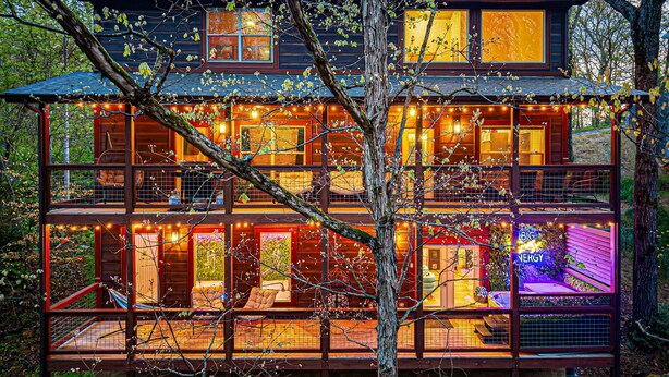 A multi-story wooden house with a balcony, string lights, and a sign reading "BIG ENERGY". - Heated Pool, Arcades, Hot Tub, Sauna, Dolly Vibes (sevierville)