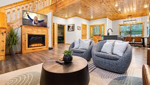 A spacious living room with a fireplace, comfortable seating, a television, and a view of the outdoors. - Heated Pool, Arcades, Hot Tub, Sauna, Dolly Vibes (sevierville)