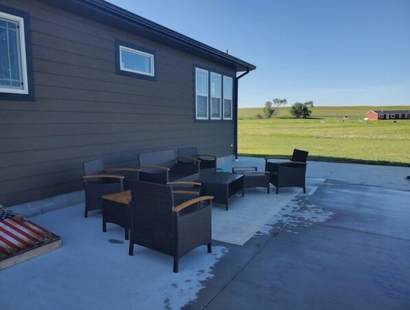 An outdoor patio with wicker furniture and a view of a grassy field.
