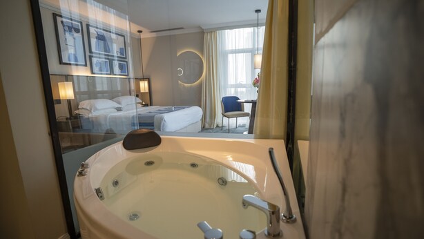 Una habitación de hotel con una bañera grande, una cama, un escritorio y una silla.