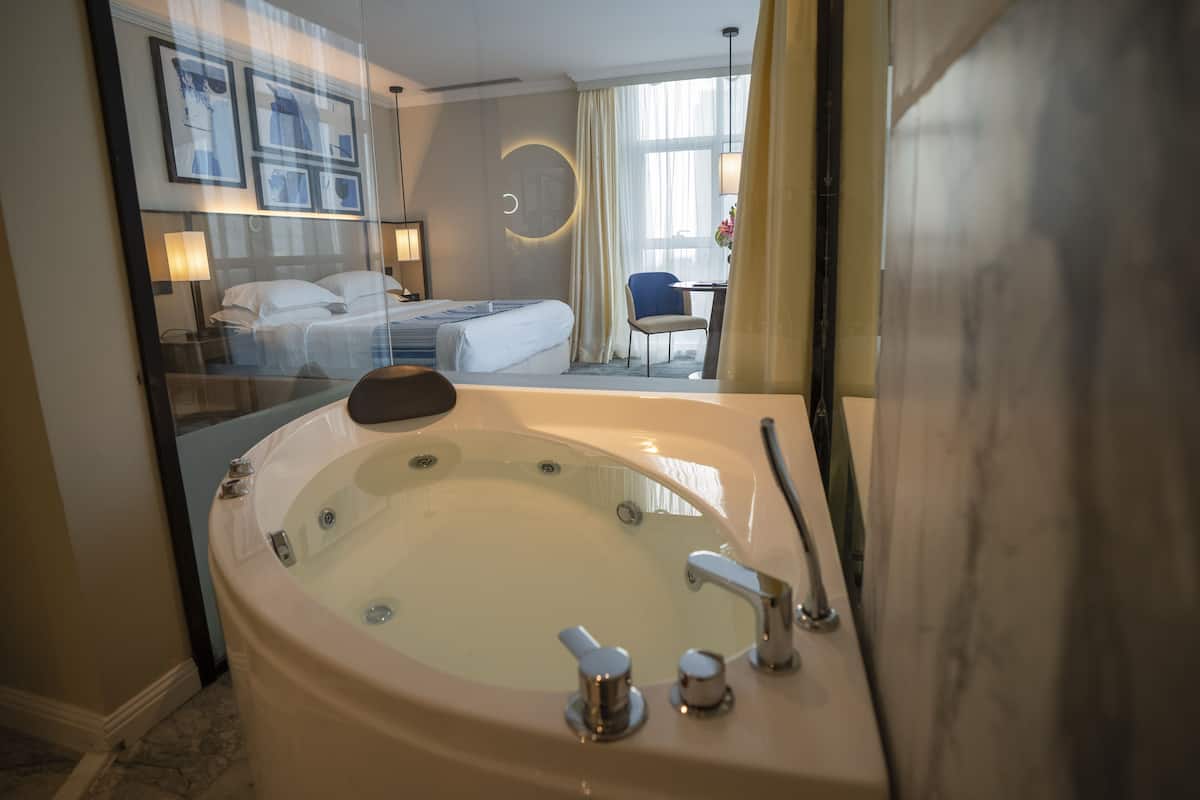 A hotel room with a large bathtub, a bed, a desk, and a chair.