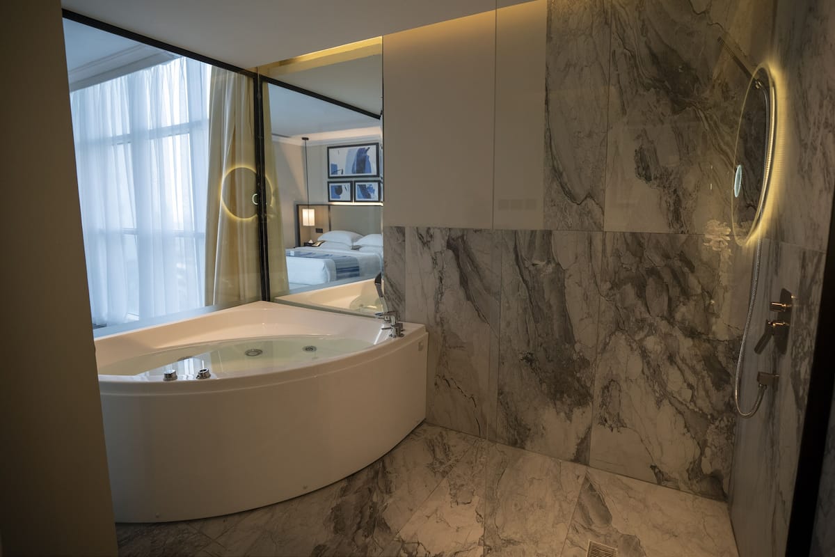A modern bathroom with a large bathtub, marble walls, and a large mirror.