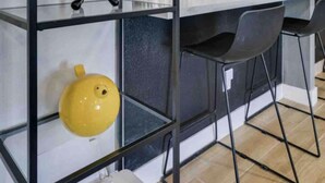 Een moderne keuken met een centraal eiland, zwarte stoelen en een geel decoratief object op een plank.