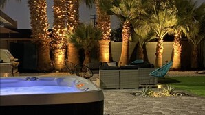 Een kuip met warm water in een goed verlicht buitengebied, met palmbomen en een terras.