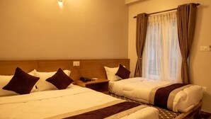 Een hotelkamer met twee bedden, een houten hoofdbord, een nachtkastje met telefoon en een raam met gordijnen.