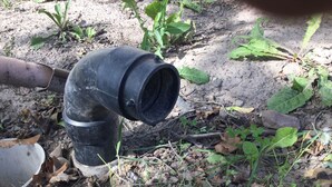 A black PVC pipe with a white pipe attached to it, lying on the ground among leaves and small plants. - RV hookup in small Montana town next to city park Address: 202 Oak (Plains)