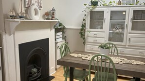 Un coin repas avec une cheminée, des chaises vertes, une table en bois et un buffet blanc aux portes vitrées.