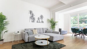 A modern living room with a grey sofa, a round coffee table, and a large window providing a view of greenery. - Central and quiet design apartment Berlin (Berlin)