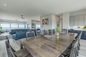 Een ruime woonkamer met een grote houten eettafel, blauwe banken en uitzicht op de oceaan.