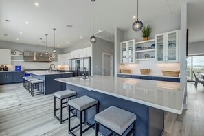 A modern kitchen with a large island, bar stools, and pendant lighting.