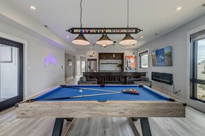 A pool table in a modern room with a bar area and large windows.