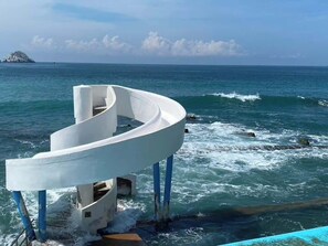 A white, curved structure extending into the sea with a rocky shoreline in the background.