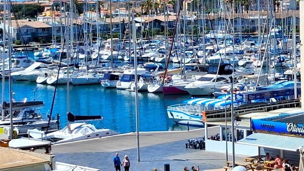 Uma marina com vários barcos atracados, uma área de estar coberta e vista dos edifícios ao redor.