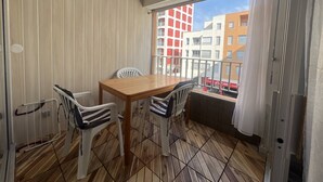 Uma varanda com mesa de madeira e quatro cadeiras, vista para edifícios, e uma cadeira listrada.