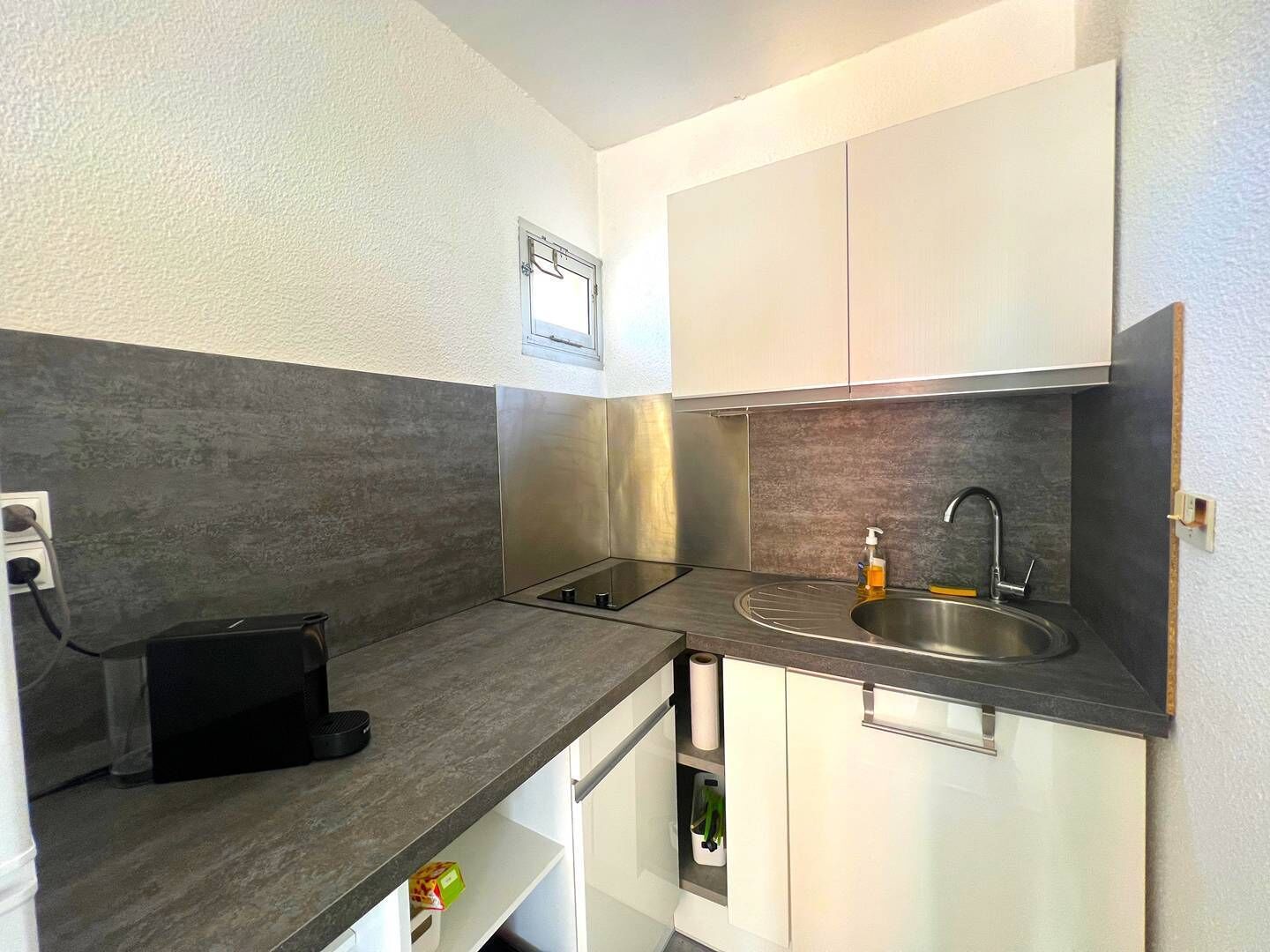 Una cocina compacta con estufa integrada, lavamanos y armarios blancos.