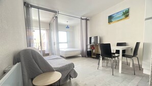 Quarto com cama, escrivaninha e cadeira. Há uma janela com cortinas, um quadro na parede e uma pequena mesa.