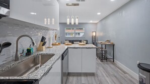 A modern kitchen with a granite countertop, stainless steel sink, and white cabinetry. - Boho Villa B (Tampa)