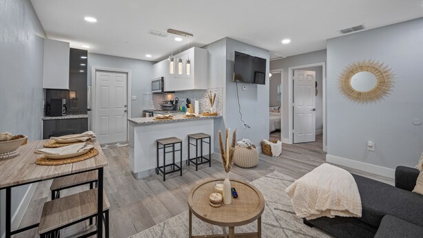 A modern kitchen with a central island, bar stools, and a dining table with a woven placemat. - Boho Villa B (Tampa)