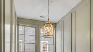 Ein Flur mit Treppe, einer Chandelierleuchtre und botanischen Drucken in Rahmen an der Wand.