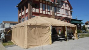 Een gebouw met twee verdiepingen en een balkon, met een beige tent ervoor.