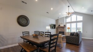 A dining area with a wooden table and chairs, a clock on the wall, and a fireplace in the background. - New Build 3BR Branson Condo w/ Arcade + Indoor Pool | FH G-303 (Branson)