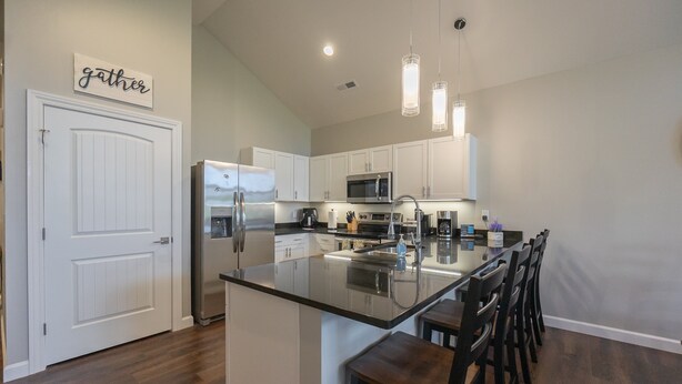 A modern kitchen with white cabinets, stainless steel appliances, a large island with bar stools, and pendant lighting. - New Build 3BR Branson Condo w/ Arcade + Indoor Pool | FH G-303 (Branson)