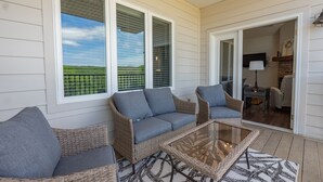 A covered patio area with wicker furniture and a glass table, overlooking a green landscape. - New Build 3BR Branson Condo w/ Arcade + Indoor Pool | FH G-303 (Branson)